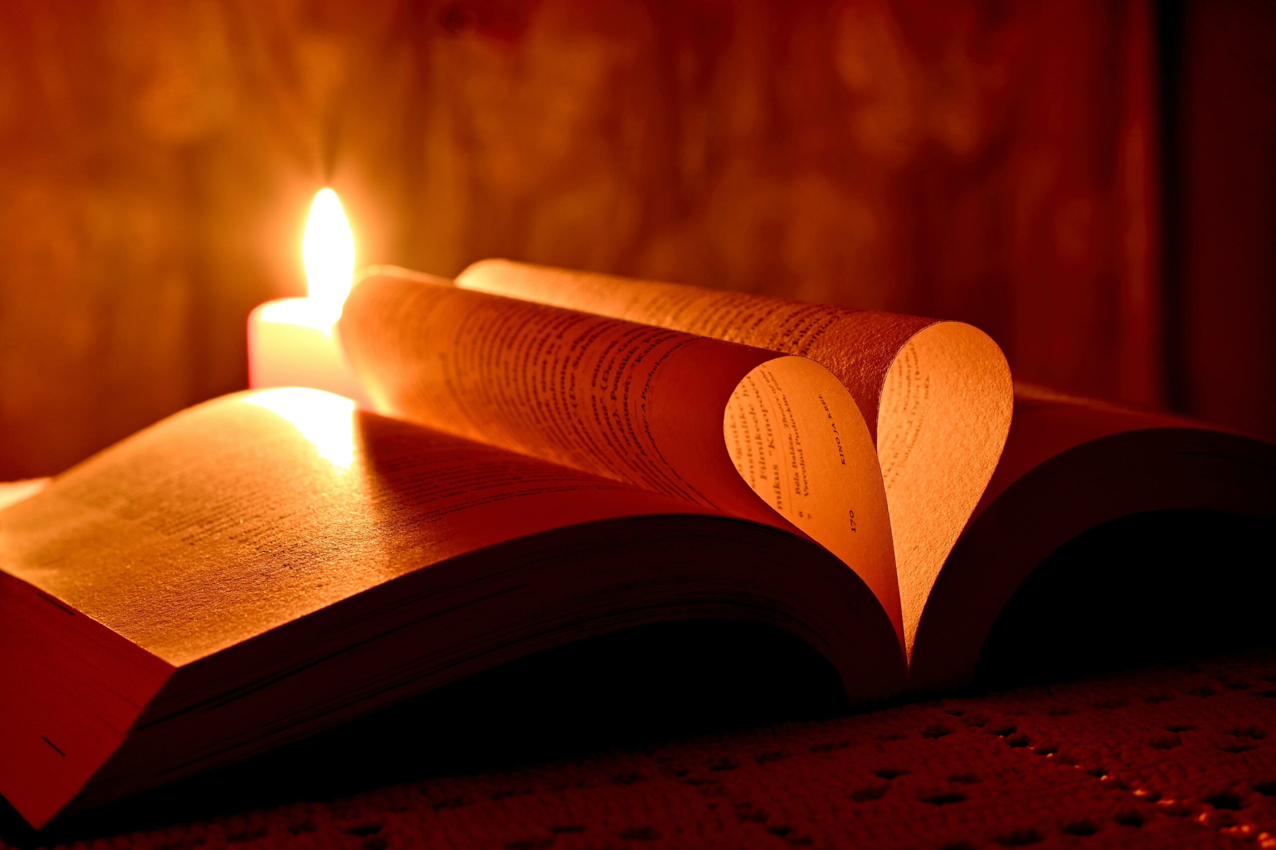 a burning candle beside a bible with pages folded over to make a heart shape
