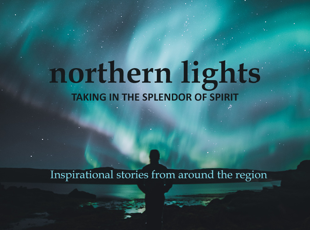 man standing on edge of lake looking at northern lights in air.