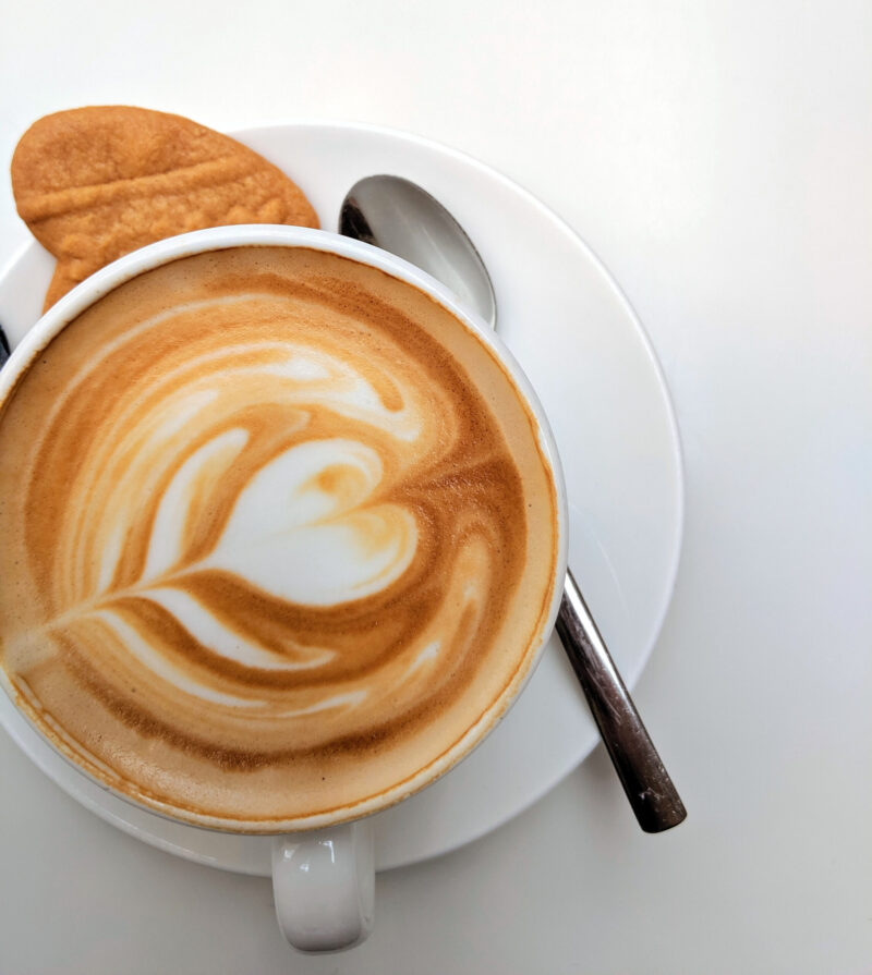 cup of latte with heart design in foam, spook and cookie on saucer